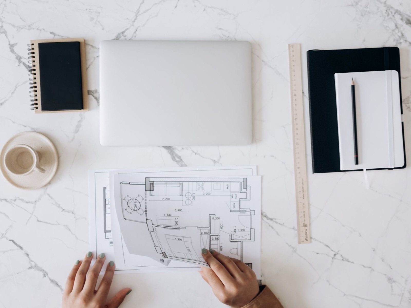 Plano de una unidad sobre una mesa de mármol, con laptop, regla y cuaderno: Mármol está en etapa de proyecto