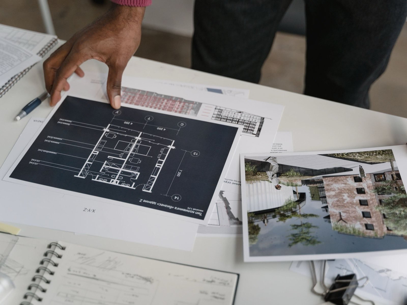 Manos revisando un plano y renders impresos sobre una mesa de trabajo: Narciso está en etapa de proyecto